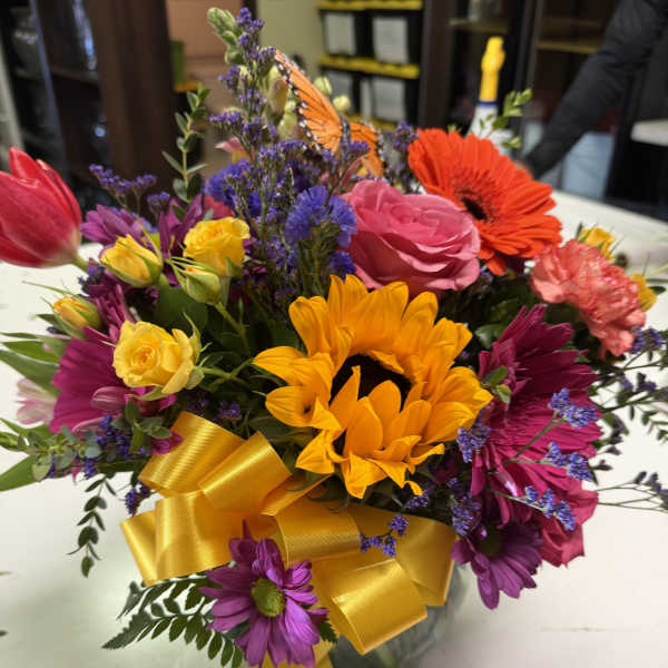 Colorful mixed bouquet with sunflowers, roses, and daisies in a glass vase