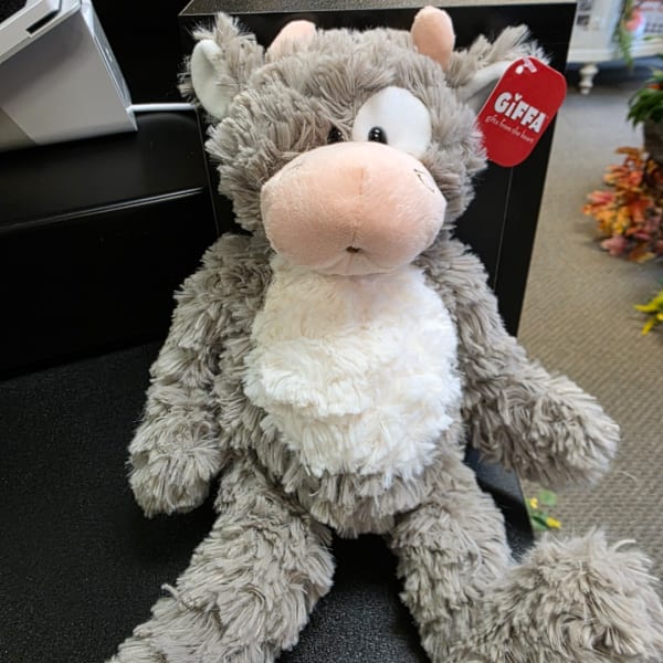 Plush gray-and-white cow with a red gift tag sitting on a black chair