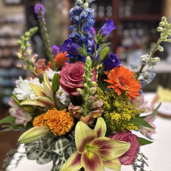 Mixed bouquet with pink roses, orange gerberas, and lilies in a plaid wrap