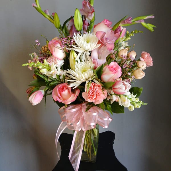 Pink and white mixed bouquet in a clear glass vase with a pink ribbon