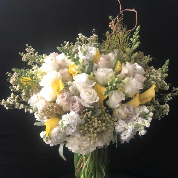 Bouquet of white and pale pink roses with yellow calla lilies in a glass vase