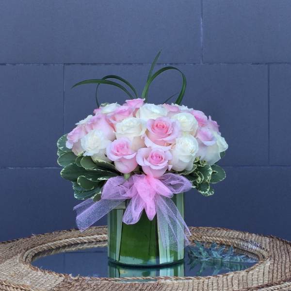 Pink and white roses arranged in a glass vase with a pink ribbon