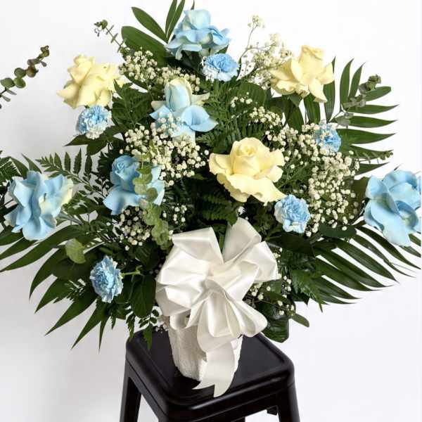 Blue and yellow rose arrangement with white ribbon in a vase