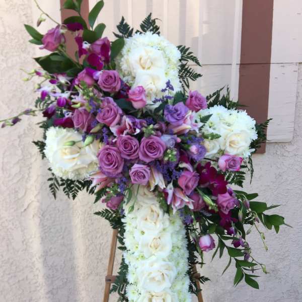 Cross-shaped floral tribute with white roses and purple flowers on an easel