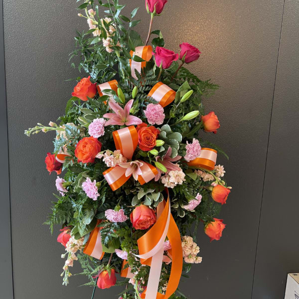 Tall floral standing arrangement with orange and pink roses, lilies, and ribbons