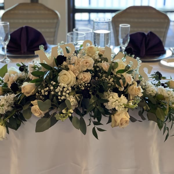 Cream rose centerpiece with greenery and table letters on a banquet table