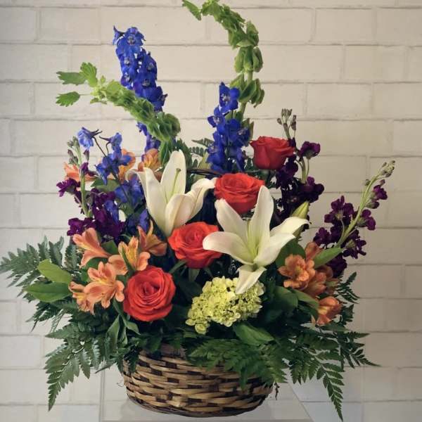 Basket arrangement with red roses, white lilies, and blue delphinium