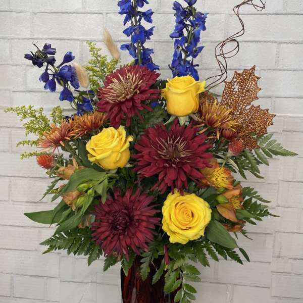 Mixed bouquet in a burgundy vase with yellow roses and blue delphinium