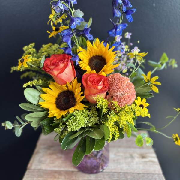 Bouquet with sunflowers, coral roses, and blue delphinium in a glass vase