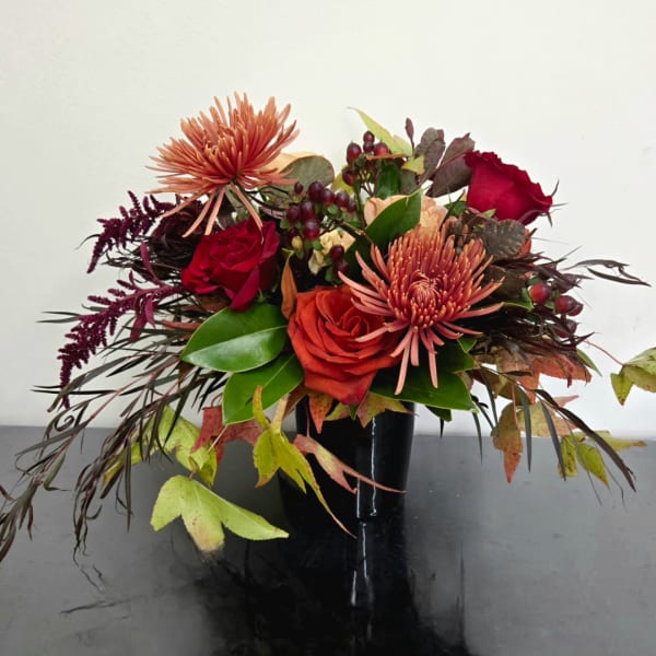 Autumn bouquet of red roses and peach mums in a black vase