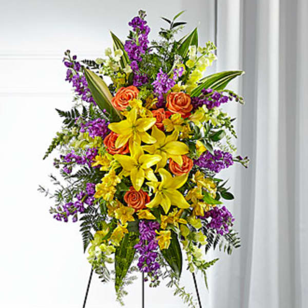 Tall floral spray with yellow lilies, orange roses, and purple flowers on a stand