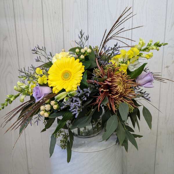Mixed bouquet with yellow gerbera, lavender roses, and chrysanthemums in a glass vase