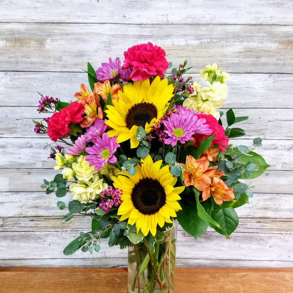 Mixed bouquet with sunflowers, pink and orange blooms in a glass vase