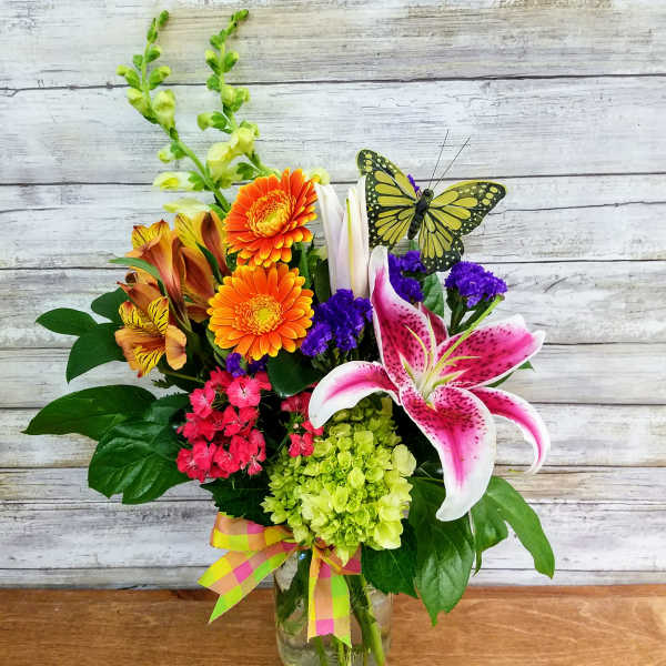 Mixed bouquet in a glass vase with orange gerberas, pink lily, and purple accents