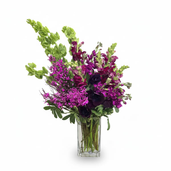 Tall arrangement of purple and green flowers with bells of Ireland and snapdragons in a clear glass vase