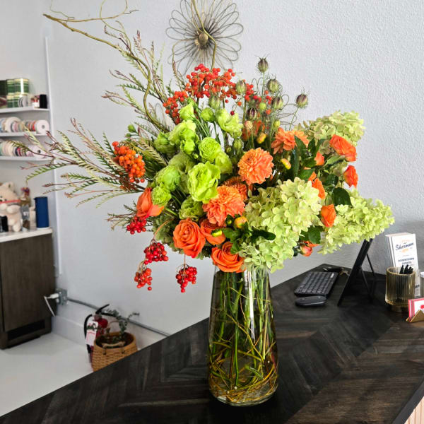 Orange roses and green blooms in a tall glass vase