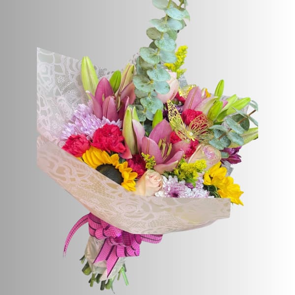 Mixed bouquet with pink lilies, sunflowers, carnations, and chrysanthemums wrapped in patterned paper