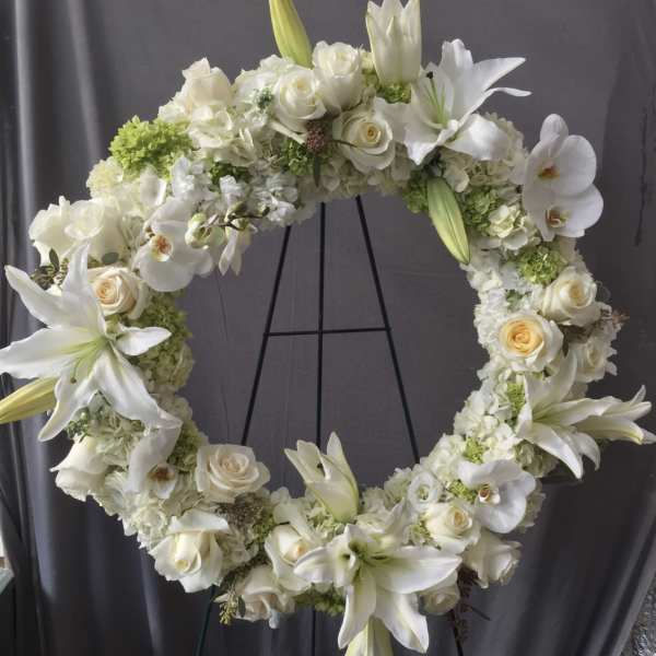 White floral wreath with roses and lilies on a black stand