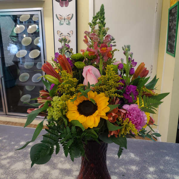 Mixed bouquet with a sunflower, pink rose, and purple blooms in a dark vase