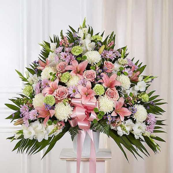 Fan-shaped pastel arrangement with pink lilies and roses, white mums, and a pink ribbon in a white container