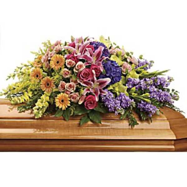 Multicolored casket spray with pink lilies, roses, yellow daisies, and purple flowers on a wooden casket