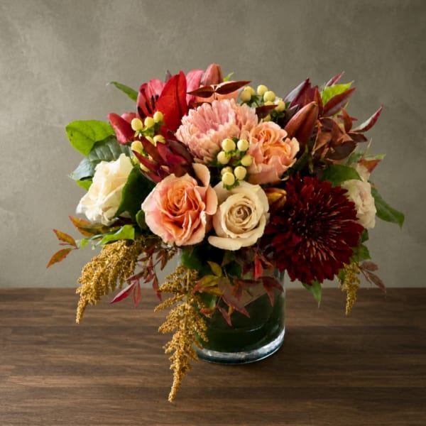 Mixed bouquet of roses, chrysanthemums, and lilies in a glass vase