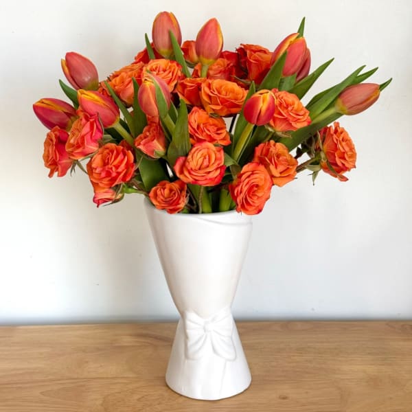 Orange roses and tulips arranged in a white vase