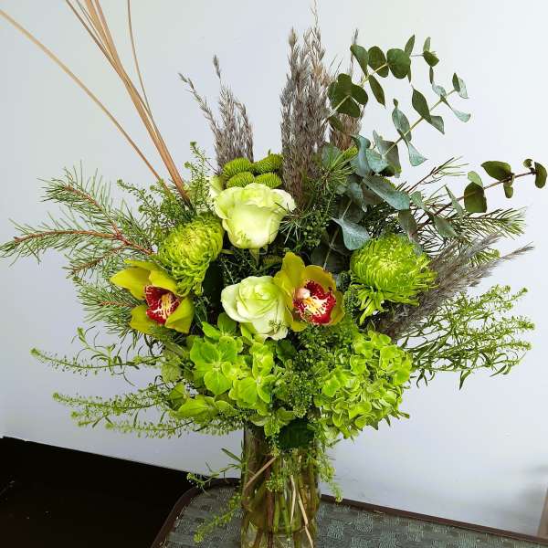 Green floral arrangement in a glass vase with orchids and hydrangeas