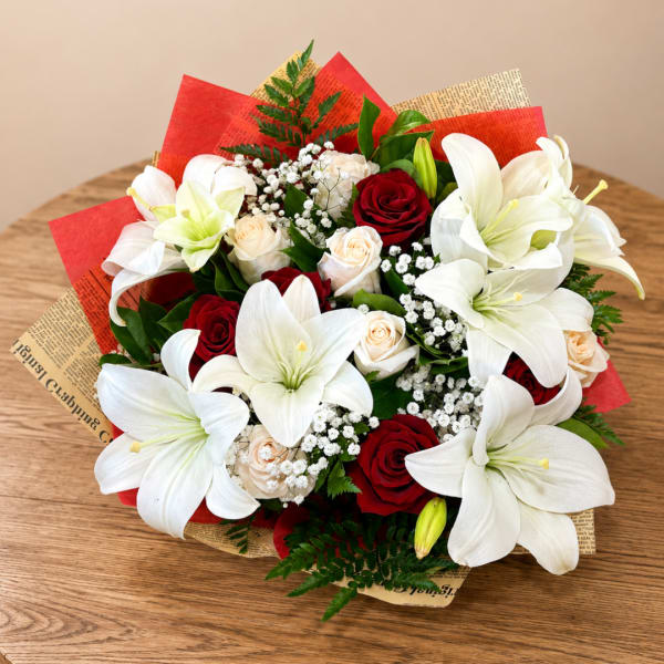 Bouquet of white lilies and red roses wrapped in red and tan paper