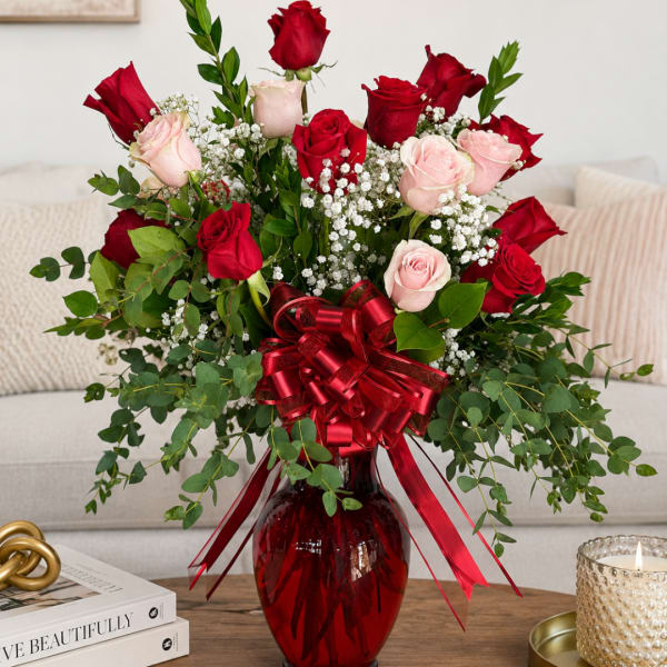 Red and pink roses arranged in a red glass vase with a ribbon bow