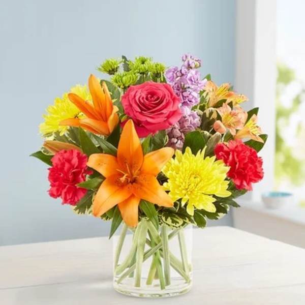 Colorful bouquet of roses, lilies, and mums in a clear glass vase