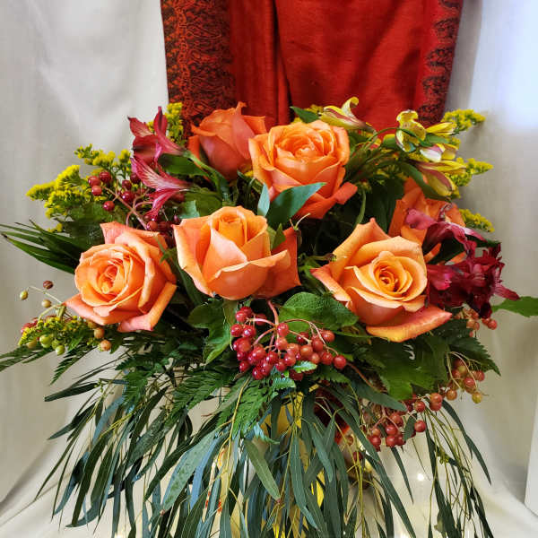 Orange roses arranged with red berries and greenery in a vase