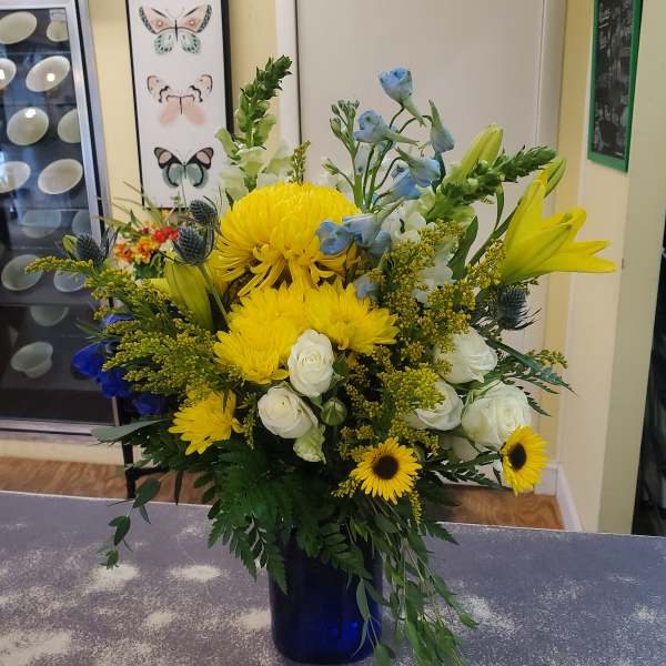 Mixed bouquet with yellow chrysanthemums, white roses, blue flowers, and lilies in a blue vase
