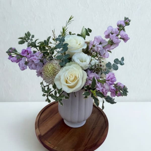 White roses and lavender flowers in a ribbed vase on a wooden tray