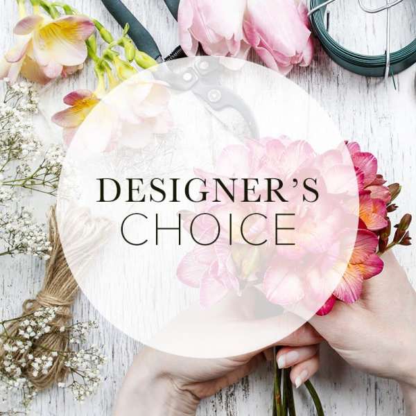 Hands holding a pink floral bouquet with a designer's choice label
