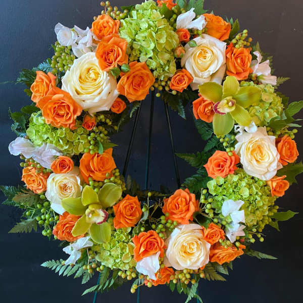 Circular floral wreath with orange and white roses and green orchids on a stand
