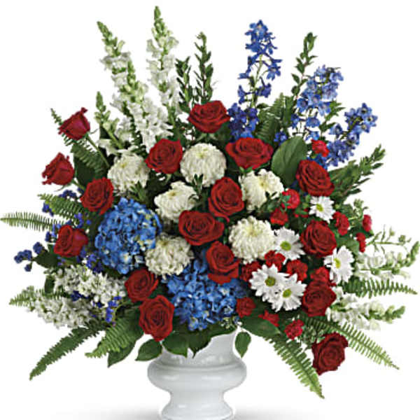 Red roses, white flowers, and blue blooms in a white urn vase