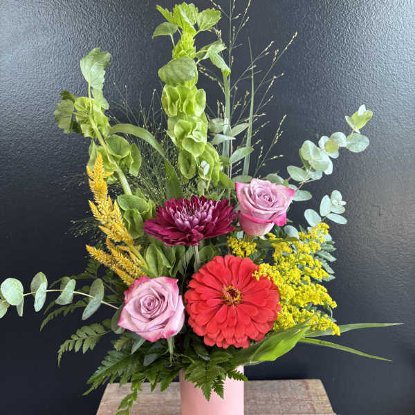 Mixed bouquet in a pink vase with roses, a red zinnia, and yellow filler flowers