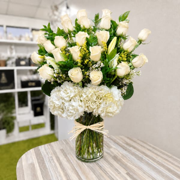White roses and hydrangeas in a clear glass vase with a raffia bow