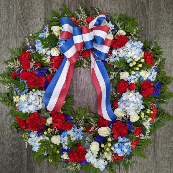 Circular floral wreath with red, white, and blue flowers and a ribbon bow
