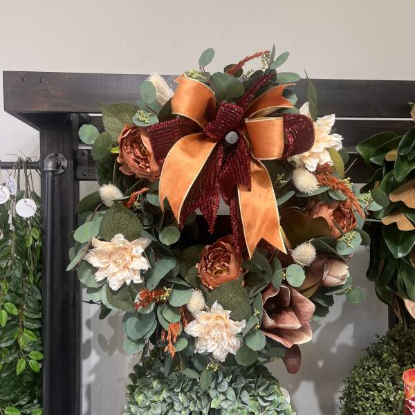 Fall wreath with orange ribbon, cream flowers, and eucalyptus on a dark frame