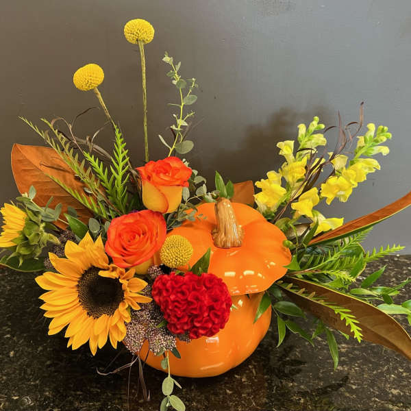 Orange pumpkin-shaped vase with sunflowers, roses, and yellow blooms