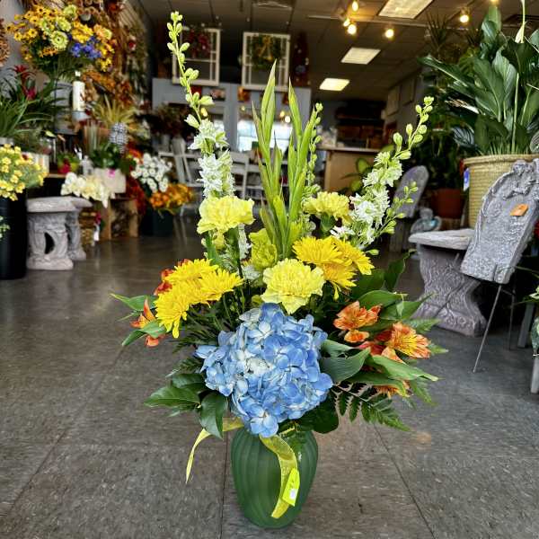 Tall mixed flower arrangement in a green vase with blue hydrangea and yellow blooms