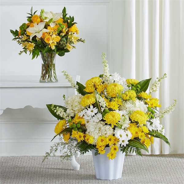 Two yellow and white floral arrangements in vases, one tall and one low.