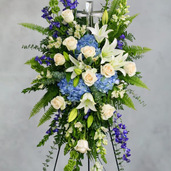 Standing floral spray with white lilies, cream roses, blue hydrangeas, and purple flowers
