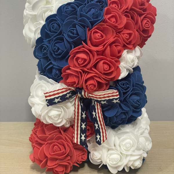 Patriotic teddy bear made of red, white, and blue roses with a ribbon bow