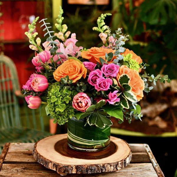Mixed bouquet of pink and orange flowers in a green glass vase