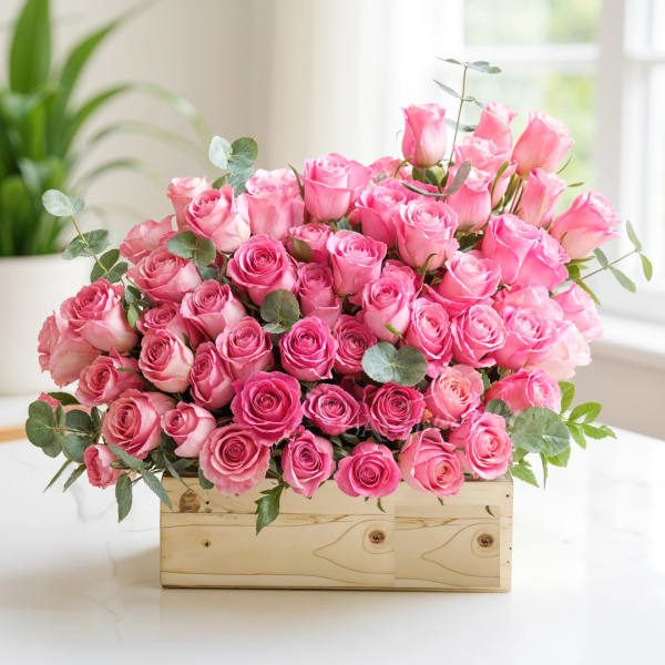 Pink roses arranged in a wooden box with eucalyptus accents