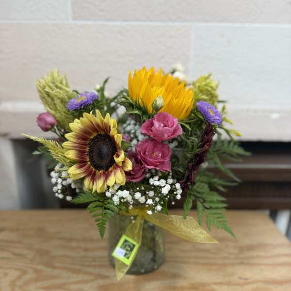 Mixed bouquet with sunflowers, pink blooms, and purple flowers in a glass jar