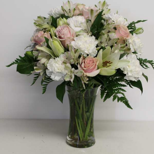 Pastel bouquet of white lilies, carnations, and pink roses arranged in a clear glass vase
